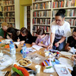 na zdjęciu widać osoby siedzące wokół stołu w sali bibliotecznej i wykonujące obrazy z filcu
