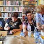 na zdjęciu widać seniorki siedzące wokół stołu w sali bibliotecznej