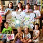 na zdjęciu widać dzieci stojące w sali bibliotecznej. Trzymają wykonane prace plastyczne.