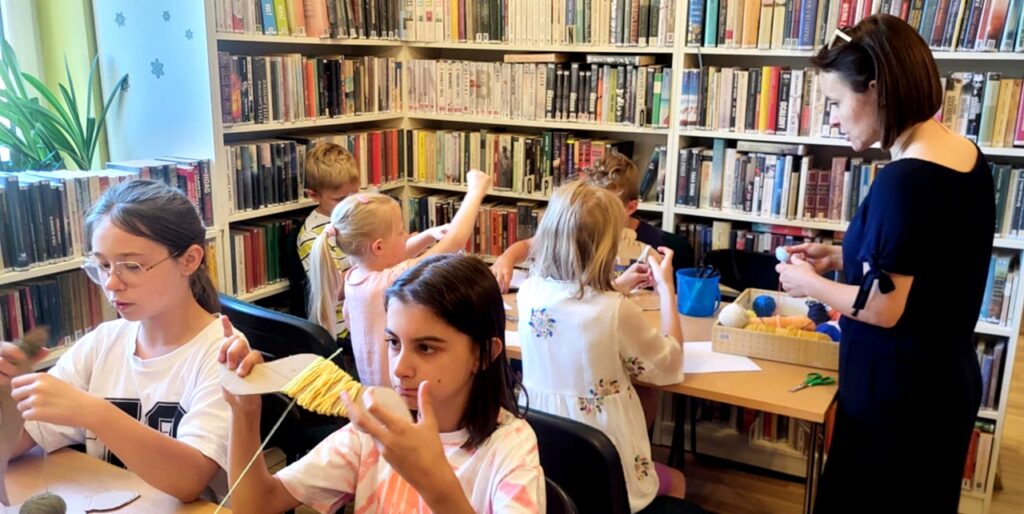 na zdjęciu widać dzieci siedzące przy stole w sali bibliotecznej