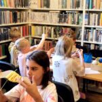 na zdjęciu widać dzieci siedzące przy stole w sali bibliotecznej