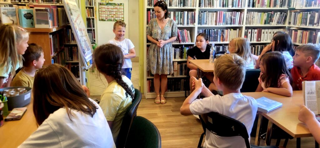 na zdjęciu widać dzieci siedzące przy stole w sali bibliotecznej