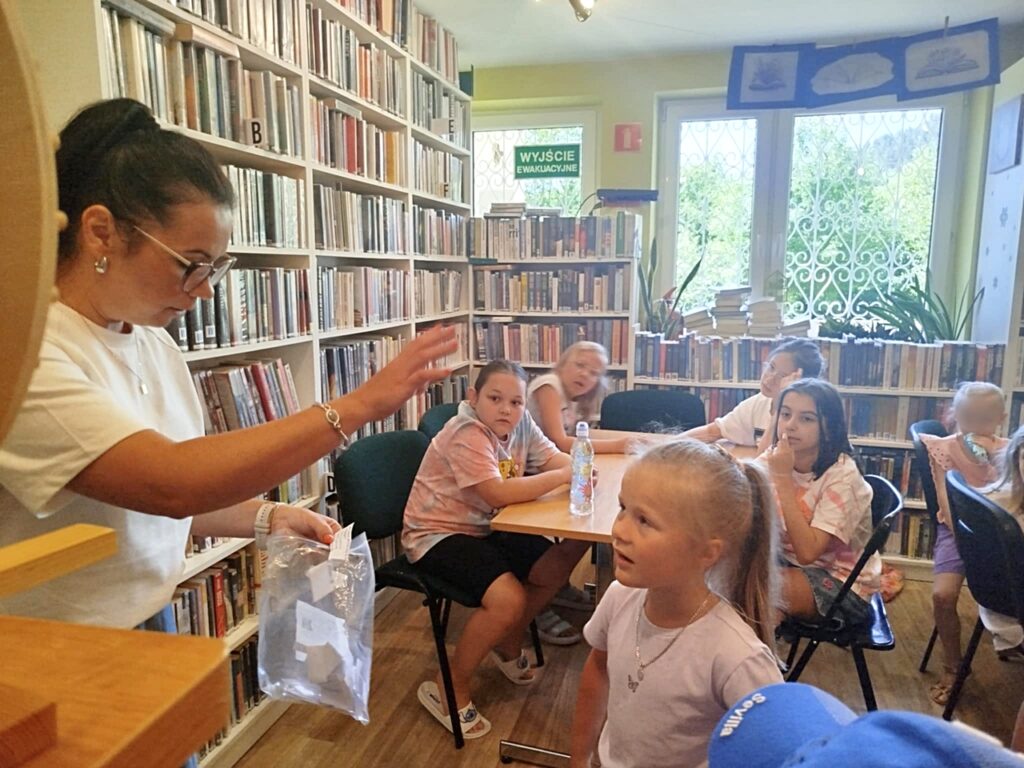 na zdjęciu widać dzieci siedzące przy stole w sali bibliotecznej