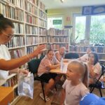 na zdjęciu widać dzieci siedzące przy stole w sali bibliotecznej