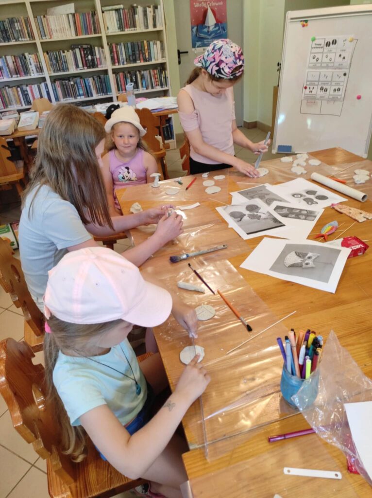 cztery dziewczynki w wieku szkolnym siedzą przy stole i wykonują prace plastyczne.