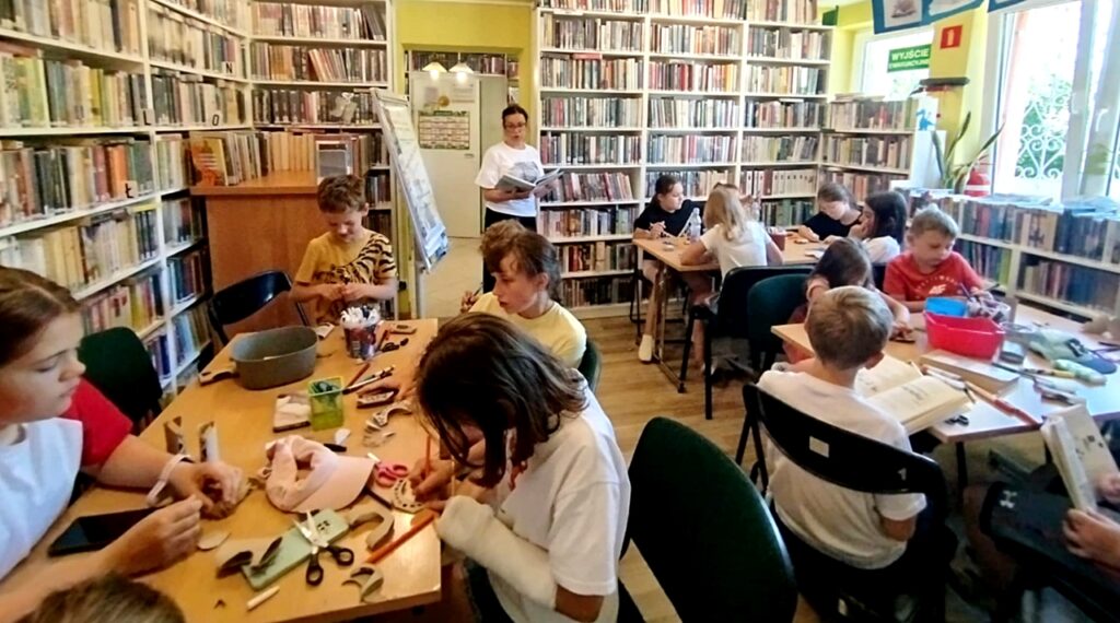 na zdjęciu widać dzieci siedzące przy stole w sali bibliotecznej