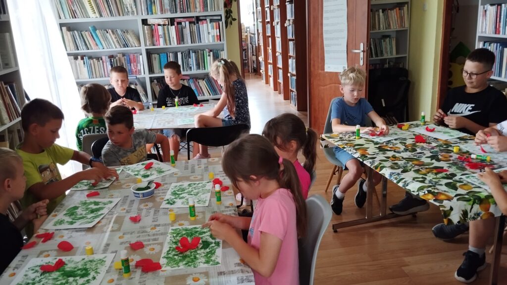 Na zdjęciu przy trzech stołach siedzą uczestnicy warsztatów i wykonują prace plastyczną