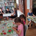 Na zdjęciu przy trzech stołach siedzą uczestnicy warsztatów i wykonują prace plastyczną