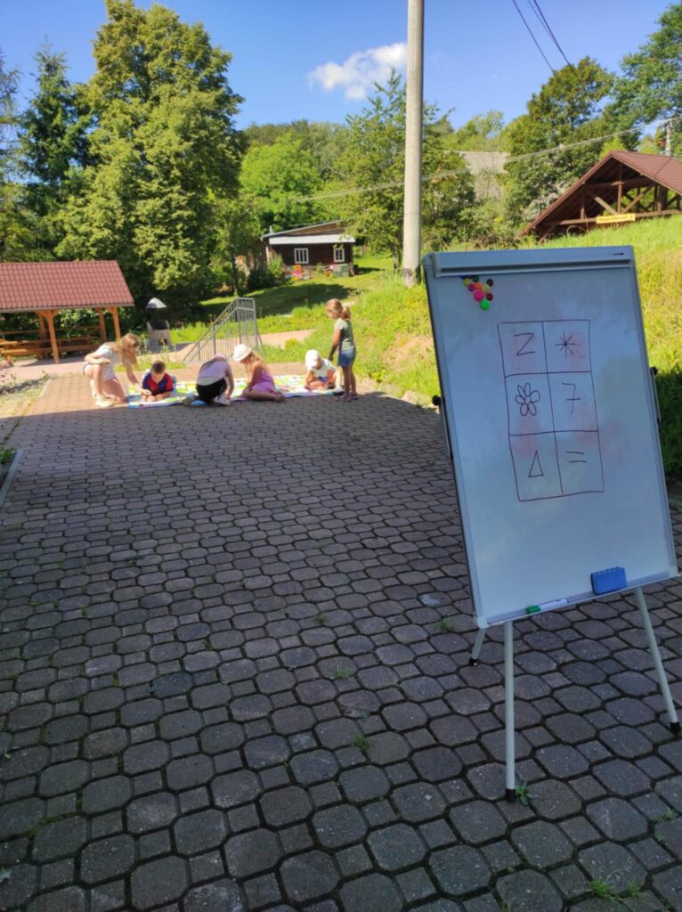 Na pierwszym planie fliphart w tyle piątka dzieci siedza na macie i rozwiązuja rebusy