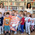 na zdjęciu widać dzieci stojące w sali bibliotecznej na tle regału z książkami