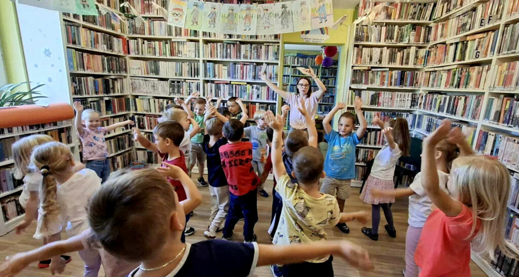 na zdjęciu widać dzieci w sali bibliotecznej wykonujące gimnastykę