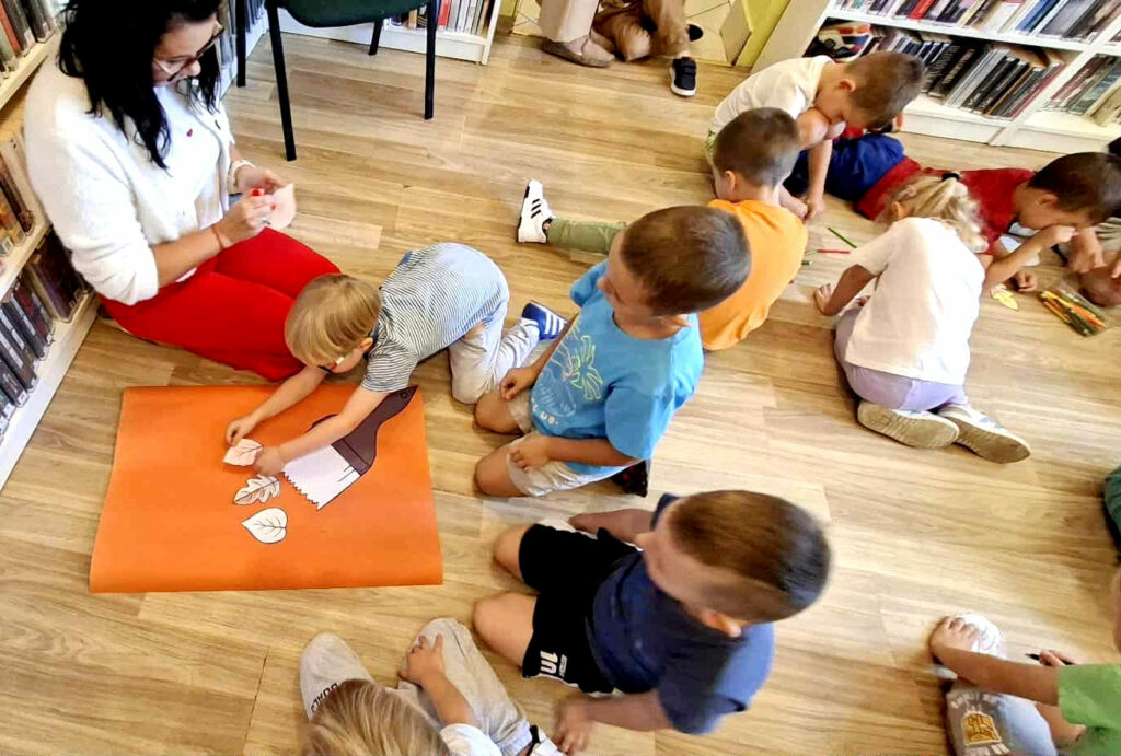 na zdjęciu widać dzieci siedzące na podłodze i kolorujące liście