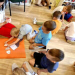 na zdjęciu widać dzieci siedzące na podłodze i kolorujące liście