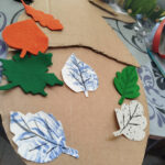 Na stole tektura na niej jesienne liście wykonane z kartonu i filcu