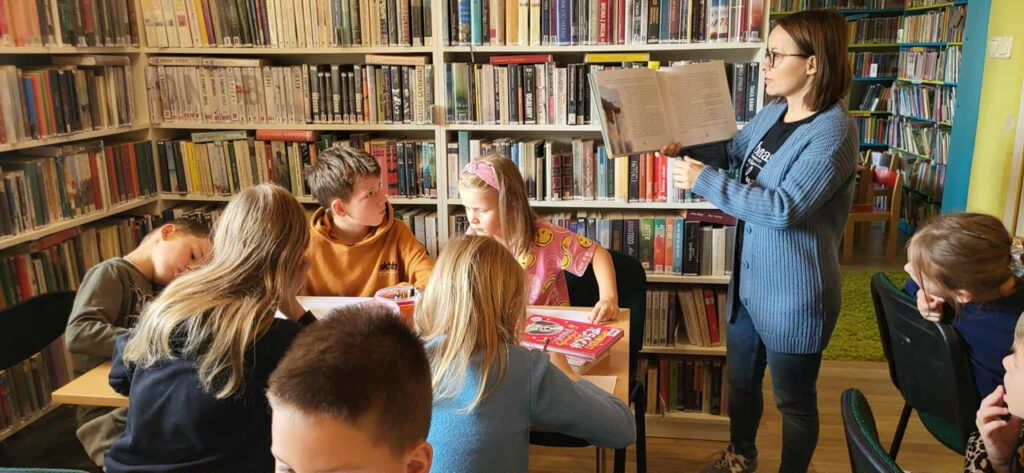 na zdjęciu widać dzieci siedzące przy stole w sali bibliotecznej