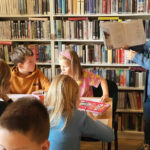 na zdjęciu widać dzieci siedzące przy stole w sali bibliotecznej