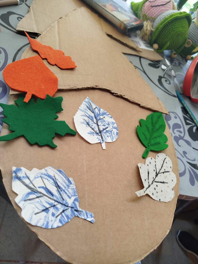 Na stole tektura na niej jesienne liście wykonane z kartonu i filcu
