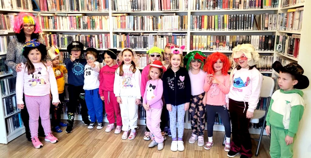 na zdjęciu widać dzieci w sali bibliotecznej w kolorowych nakryciach głowy