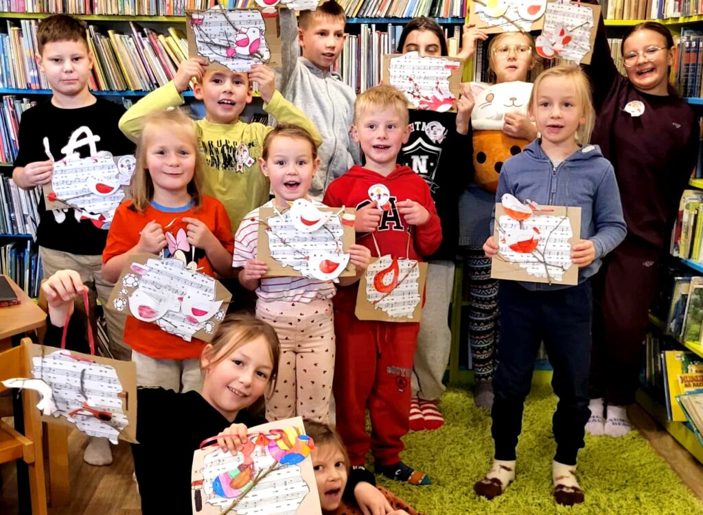 Na zdjęciu widać dzieci w sali bibliotecznej stojące na tle regału z książkami