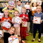 Na zdjęciu widać dzieci w sali bibliotecznej stojące na tle regału z książkami