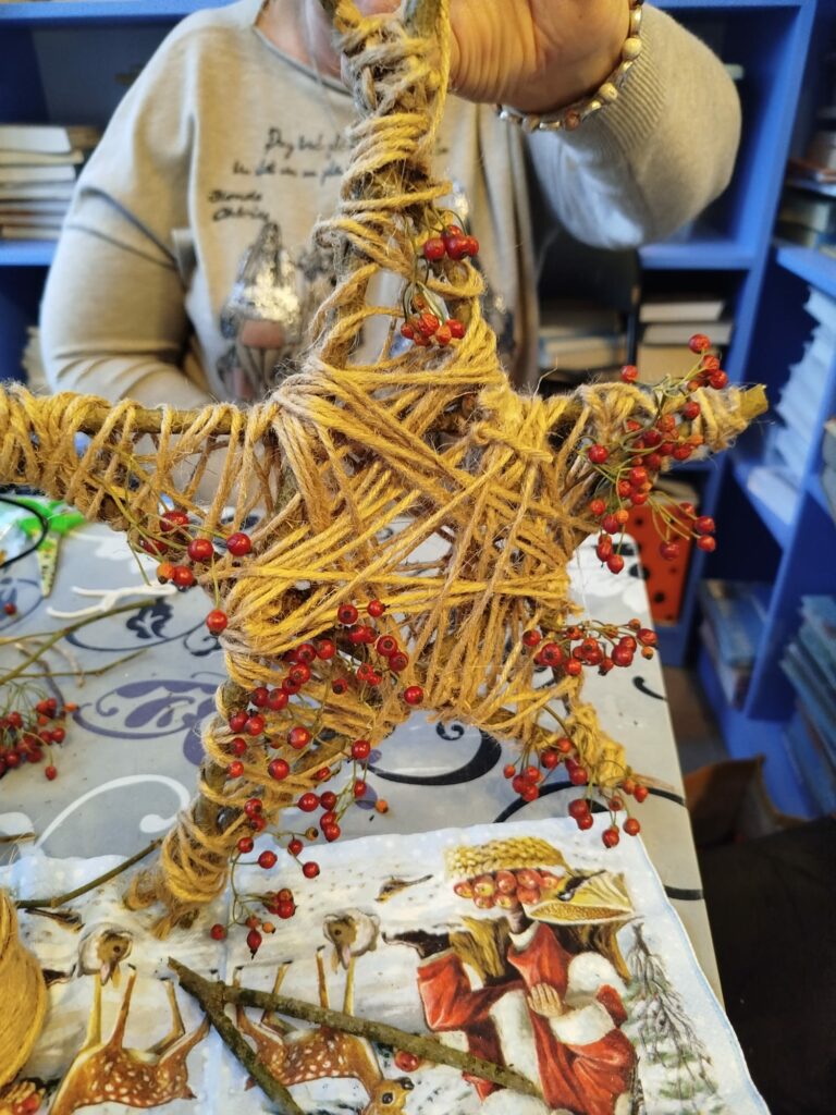 Na zdjęciu częściowo widac kobietę trzymajaca w ręku gwiazde świąteczna ozdobioną jarzębiną.