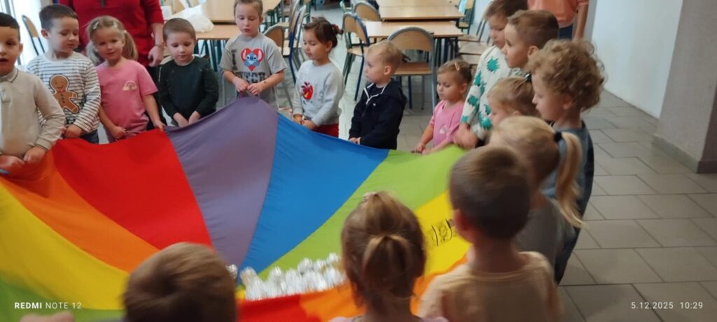 Na zdjęciu duża grupa dzieci trzyma za końce kolorową chustę klanza