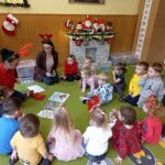 Na sielonym dywanie w sali przrdszkolnej siedza dzieci wraz z paniami bibliotekarkami, które pokazują dzioeciom książeczki kolorowe.