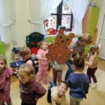 Na zdjęciu grupa dzieci trzyma w tęce kartonowego kolorowego misia. Wokół okna i kolorowe zabawki.