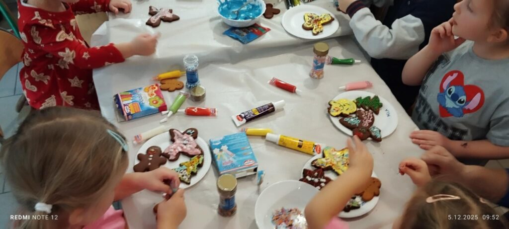 Przy stole siedza dzieci. Przed nimi na talerzykach widać pierniczkowe postacie udekorowane przez dzieci .