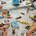 Przy stole siedza dzieci. Przed nimi na talerzykach widać pierniczkowe postacie udekorowane przez dzieci .