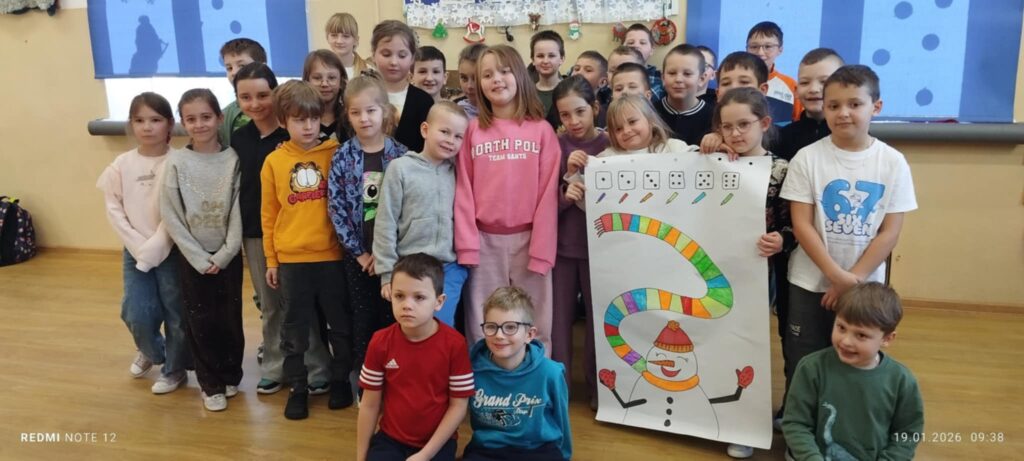 Na zdjęciu duża grupa dzieci w wieku szkolnym 1-3 klasa. Dzieci trzymają w ręku karton na którym jest Bałwan z wymalowanym kolorowym szalikiem .