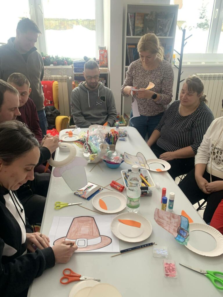 na zdjęciu stół przy którym siedzą kobiety i mężczyźni uczestniczące w warsztatch kreatywno - literackich. Na stole materiały plastyczne potrzebne do warsztatów .