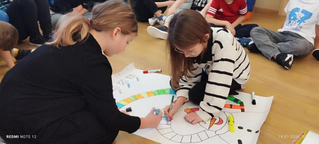 na podłdze widać dwie dziewczynki, które kolorują szalik Bałwana.