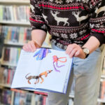 Na zdjęciu mężczyzna prezentuje książkę. Za nim regały z książkami.