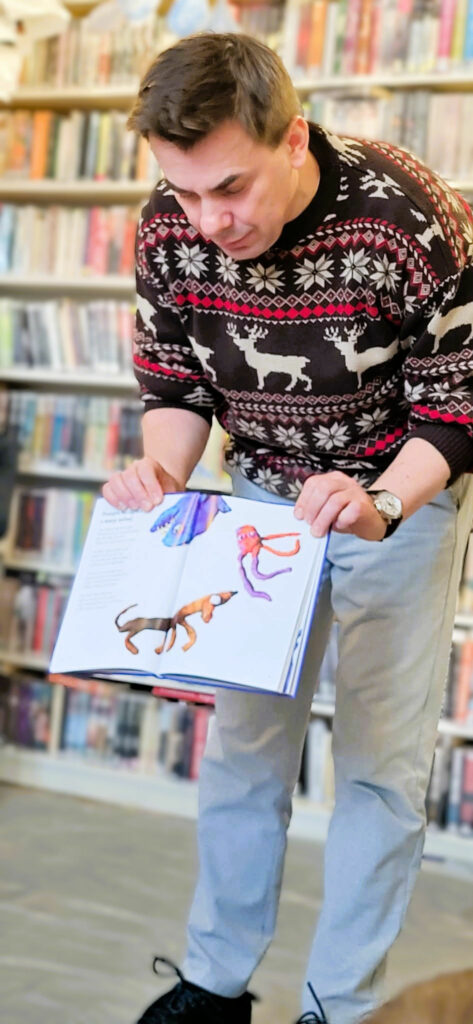 Na zdjęciu mężczyzna prezentuje książkę. Za nim regały z książkami.