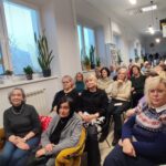 Na zdjęciu wnętrze biblioteki w którym odbywa się spotkanie autorskie z Ewą Chotomską. Na krzesłach przodem siedza osoby, które przybyły na spotkanie.