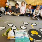 Na zdjęciu dzieci siedzące na kolorowym dywanie . Przed nimi książka o Pingwinku.