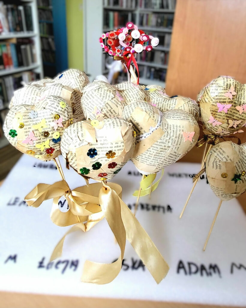 na zdjęciu stojące serca ze styropianu, oklejone kartkami zapisanymi drukiem. Dwa serca maja przewiązane złote wstążki