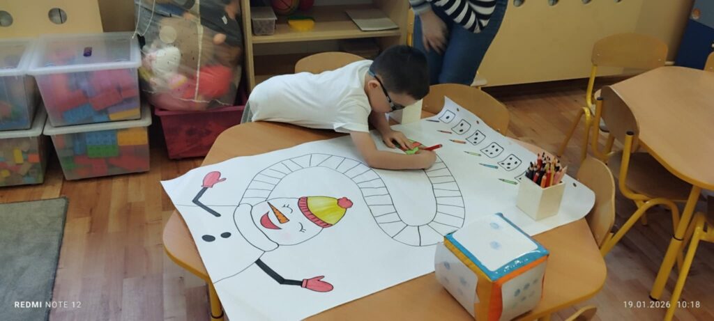 Na zdjęciu widać chłopca, który koloruje szalik Bałwana. Jakton ze szkicem Mikołaja jest na małym przedszkolnym stole.