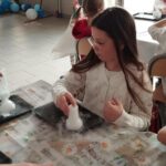 Przy stole siedzą dwie dziewczynki i wykonują eksperymenty.