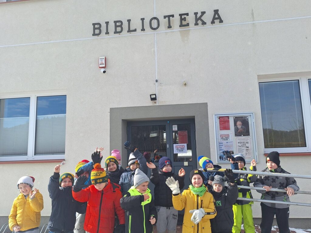 Krupa dzieci w kurtkach kolorowych i czapkach stoi przed drzwiaami biblioteki po zakończonej lekcji bibliotecznej.