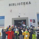Krupa dzieci w kurtkach kolorowych i czapkach stoi przed drzwiaami biblioteki po zakończonej lekcji bibliotecznej.