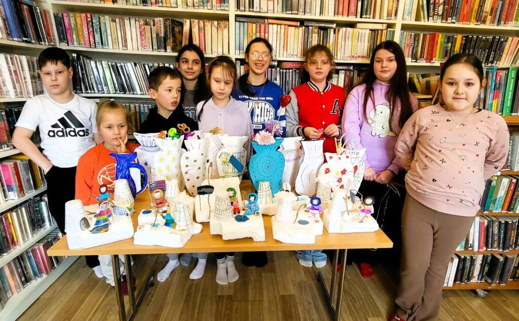 na zdjęciu widać dzieci stojące za stołem n którym poukładane są wykonane przez nie prace plastyczne