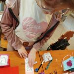 na zdjęciu dziewczynka stoi przy stole i wykonuje pracę plastyczną