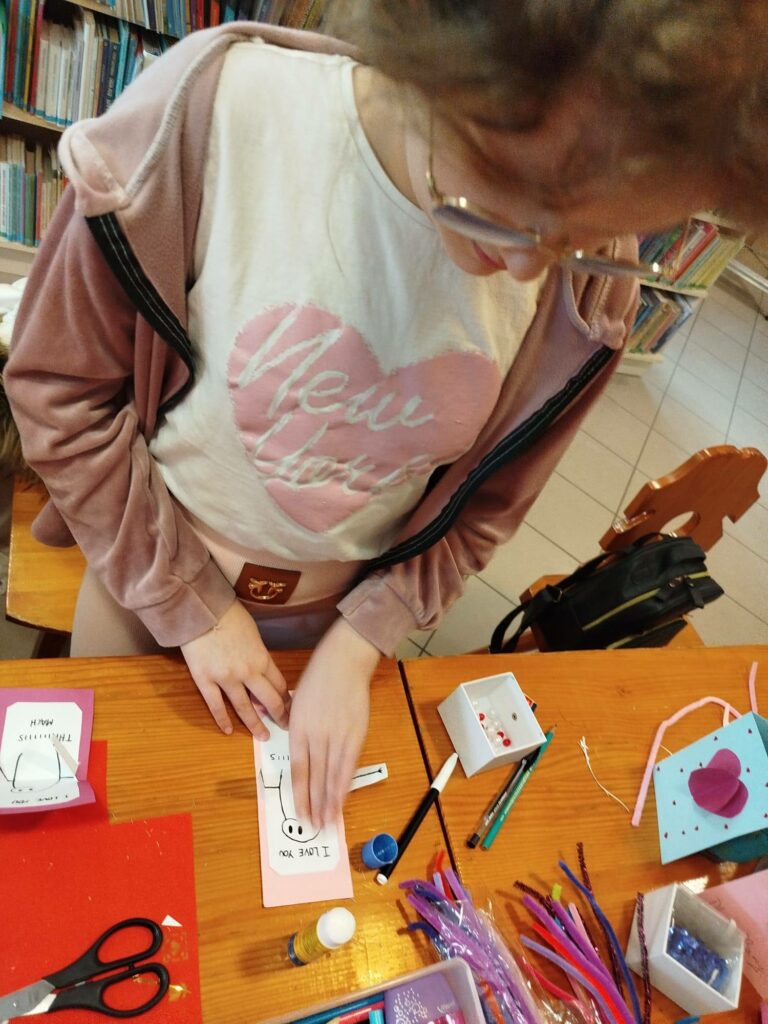 na zdjęciu dziewczynka stoi przy stole i wykonuje pracę plastyczną