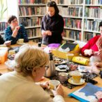 na zdjęciu widać panie seniorki siedzące wokół stołu w sali bibliotecznej i wykonujące korale