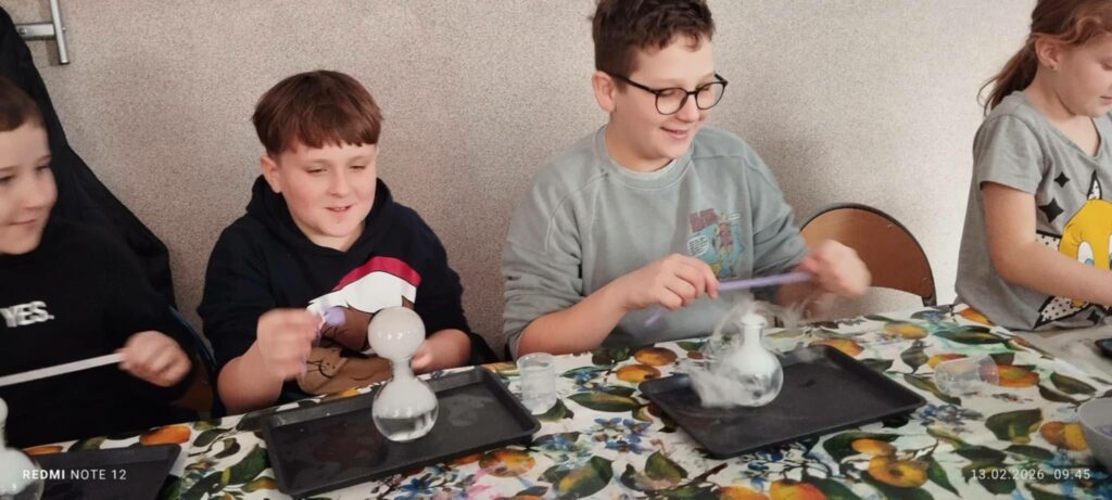 W sali bibliotecznej przy stole siedzą chłopcy i wykonują eksperymenty