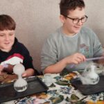 W sali bibliotecznej przy stole siedzą chłopcy i wykonują eksperymenty