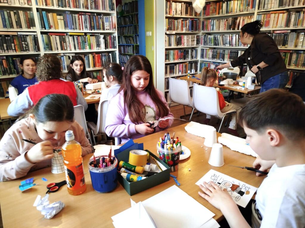 na zdjęciu widać salę biblioteczną i dzieci siedzące wokół stołu