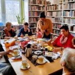 na zdjęciu widać panie seniorki siedzące wokół stołu w sali bibliotecznej i wykonujące korale